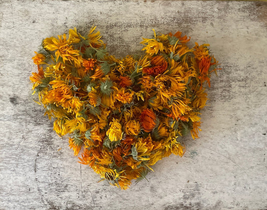 heart shape made with dried orange and yellow calendula flowers on a farmhouse white background