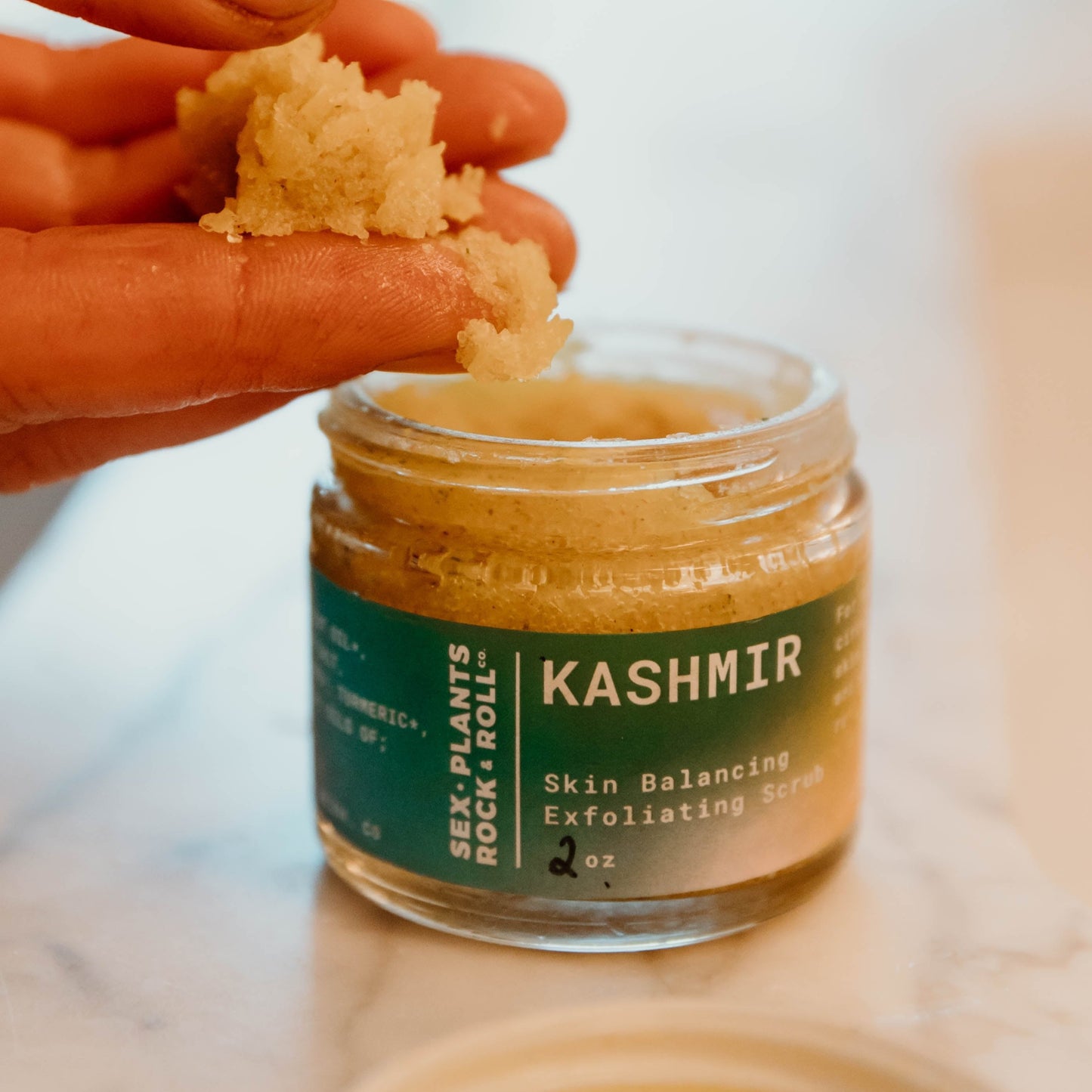 small glass jar with yellow salt and fingers holding small pile of scrub mixture