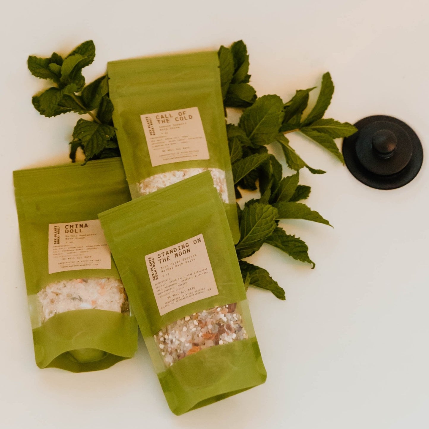 three green bags of salt and herbs on a pile of fresh mint in the bottom of the white bath tub