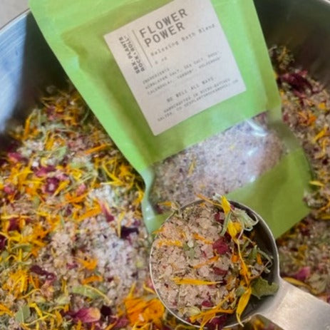 dried flowers and salt in a bowl with a silver spoon  holding the mix above a green back labeled 'flower power'